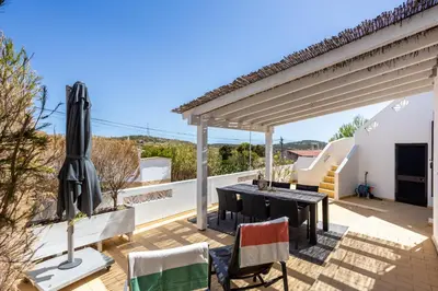 a patio with a table and chairs and an umbrella at Paraíso dos Pássaros in Budens
