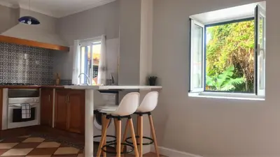a kitchen with white counter stools and a window at Casa da Avó Duca in Machico