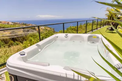 a hot tub on a balcony with the ocean at House - sleeps 3 free parking garden & jacuzzi in Estreito da Calheta