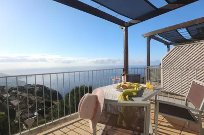a table on a balcony with a view of the ocean at Village Cabo Girao in Câmara de Lobos