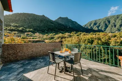 a table and chairs on a balcony with mountains at Olinda's Place by Amazing Madeira in Boaventura