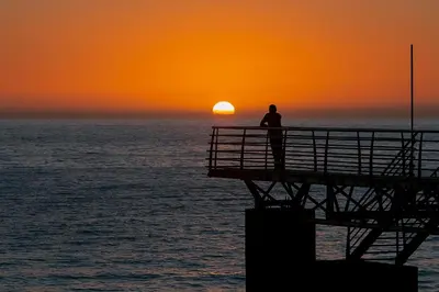 a man standing on a pier watching the sunset at Madalena Sunset by Homie in Madalena do Mar