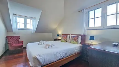 a bedroom with a bed and a chair and windows at Casa do Seixal in Seixal