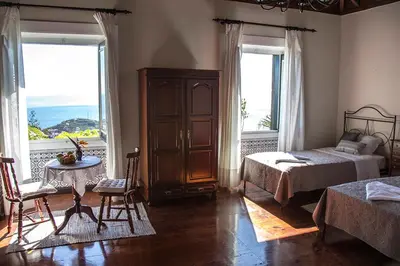 a bedroom with two beds and a table and two windows at Vila Afonso in Estreito de Câmara de Lobos