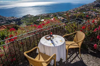 a table and chairs on a balcony with a view of the ocean at Vila Afonso in Estreito de Câmara de Lobos