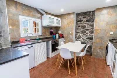 a kitchen with white cabinets and a table and chairs at Madeira Bird House - House in the Mountains With Garden in São Vicente