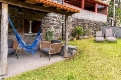 a patio with chairs and a hammock in a yard at Madeira Bird House - House in the Mountains With Garden in São Vicente
