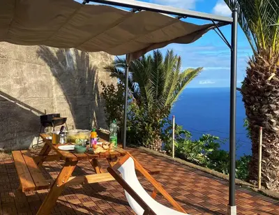 a table and chairs under an umbrella on a patio at Garajau House - Sunrise to Sunset Ocean View Villa in Caniço