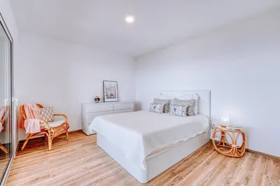 a white bedroom with a bed and a chair at Casa das Voltinhas in Ponta do Sol