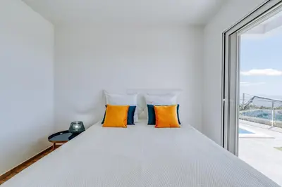 a bedroom with a bed with orange pillows and a window at Casa das Voltinhas in Ponta do Sol