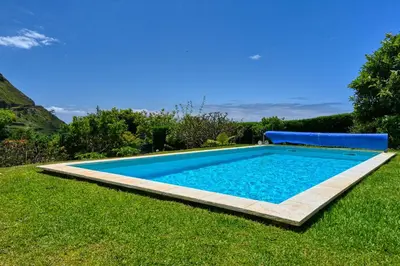 a swimming pool in a grassy yard with a blue pool at Villa Santa Madalena, a Home in Madeira in Arco da Calheta