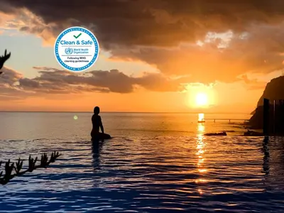 a man sitting on a surfboard in the water with a sunset at Infinity pool & Amazing Sunset Ocean View in Funchal