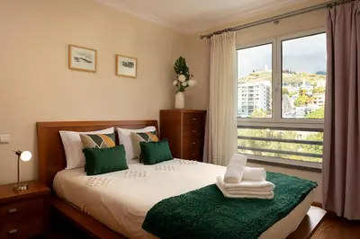 a bedroom with a bed with green pillows and a window at Margarida's Apartment com piscina e vista mar in Funchal
