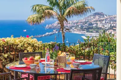 a table with a bowl of fruit and a view of the ocean at OurMadeira - Villa Vista Sol in Funchal