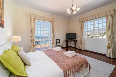 a bedroom with a large bed and two windows at OurMadeira - Villa Vista Sol in Funchal