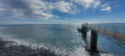 a pier in the ocean with people standing on it at Madalena Beach Tiny House in Ponta do Sol