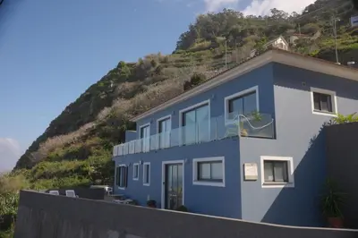 a blue house with a hill in the background at Casa Azul - Ocean View in Porto Moniz