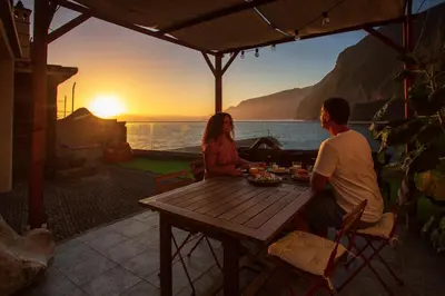 a man and a woman sitting at a table watching the sunset at Madeira Black Sand House by Stay Madeira Island in Seixal
