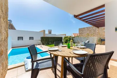 a patio with a wooden table and chairs and a swimming pool at Villa Hobie Cat in Sagres