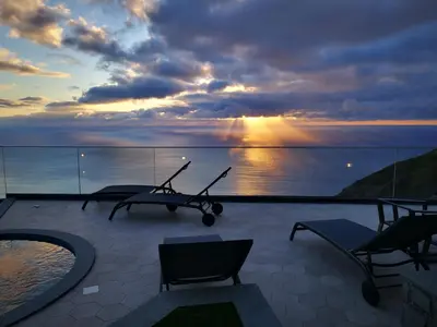 a balcony with a view of the ocean at sunset at The Cliffhouse by LovelyStay in Fajã da Ovelha