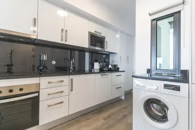 a kitchen with white cabinets and a washer and dryer at Belle Vue Résidence by Atlantic Holiday in Santa Cruz