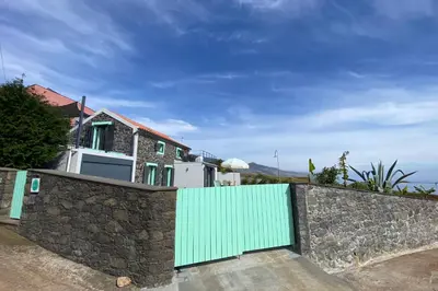 a stone wall with a green gate in front of a house at The Hideaway Madeira in Prazeres