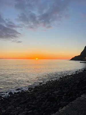 a sunset over the water with a rocky beach at Vila Feliz in Paul do Mar