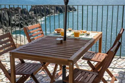 a wooden table with two chairs and a view of the water at Casa do Ilhéu - House of Ilhéu - Câmara de Lobos in Câmara de Lobos