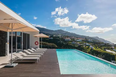 a pool with chairs and umbrellas on a house at OurMadeira - Ocean Panorama in Estreito da Calheta
