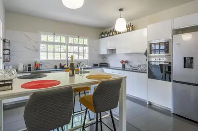 a kitchen with white cabinets and a island with chairs at VILLA LEONARDO in Caniço