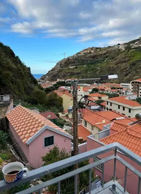 a view of a town from a balcony with a cup of coffee at Lovely newly refurbished, 1 bedroom top floor apartment with sea views, fast WI-FI CABLE TV and Netflix in Ribeira Brava