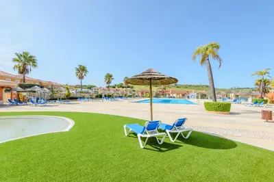 two chairs and an umbrella on the grass near a pool at Casa Sunny Days - Boavista Resort in Lagos