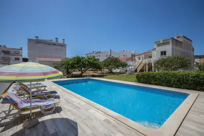 a swimming pool with two chairs and an umbrella at Villas Brites nº5 in Burgau