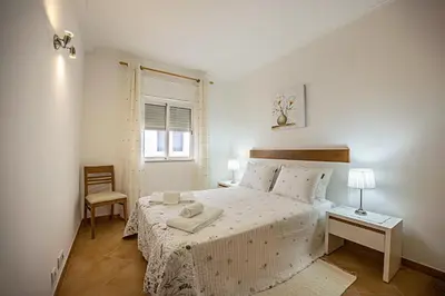 a white bedroom with a bed and a chair at Casa Bege T2 in Burgau