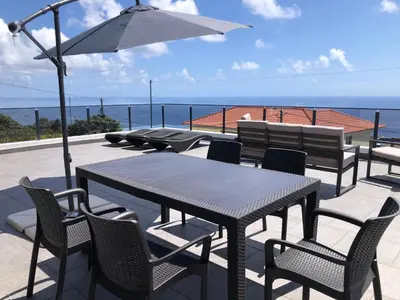 a table and chairs with an umbrella and the ocean at Calheta Ocean View Family Apartment - Air Condition in Estreito da Calheta