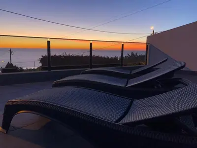 a row of chairs sitting on a balcony at sunset at Calheta Ocean View Family Apartment - Air Condition in Estreito da Calheta