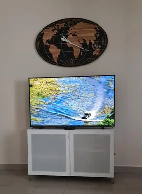 a flat screen tv sitting on a white stand with a clock at Funchal Centre Comfort in Funchal