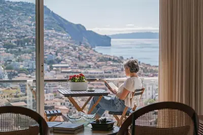 a man sitting at a table with a laptop on a balcony at Casa do Castelo by An Island Apart in Funchal
