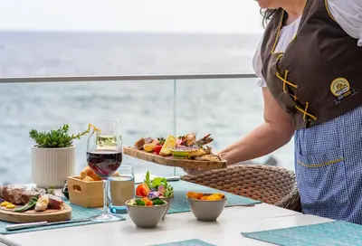a person holding a plate of food on a table with wine at Aqua Natura Madeira in Porto Moniz