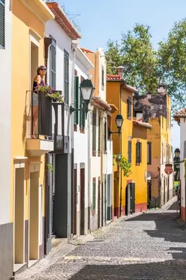 a woman on a balcony in a street with buildings at Casa Caetano by An Island Apart in Funchal