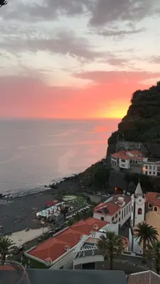 a sunset over a beach with buildings and the ocean at Casa do Avô in Ponta do Sol