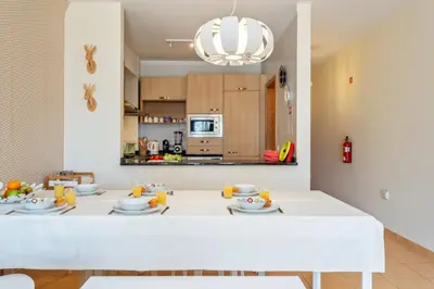 a dining room with a white table and a kitchen at Casa das Pedras Pretas - By WeHost in Porto Santo