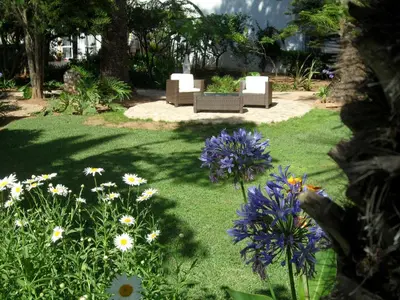 a garden with white chairs and purple and white flowers at Cozy Studio with garden view in Praia da Luz in Luz