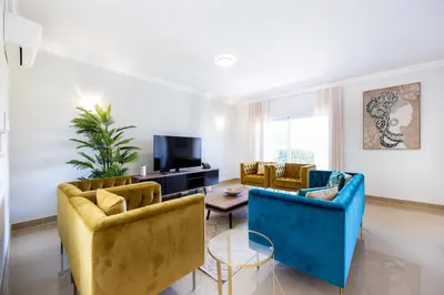 a living room with yellow and blue chairs and a table at Casa Malhotra at Boa Vista Golf Resort, Bayview Village in Lagos