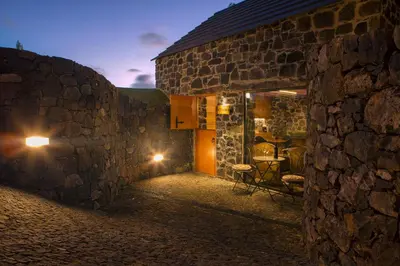a stone building with a table and chairs on a patio at Palheiros do Serrado by Real Vision in Estreito da Calheta