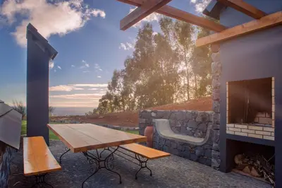 a patio with a wooden table and a fireplace at Palheiros do Serrado by Real Vision in Estreito da Calheta