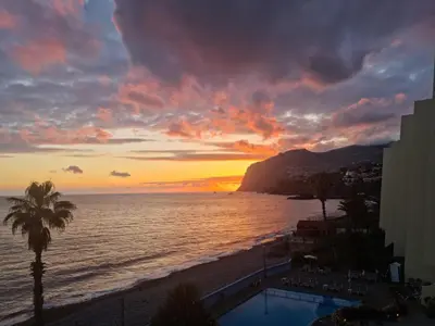 a sunset over the ocean and a beach with a resort at Tranquil Beachside Stay - Atlantic Gardens Beach in Funchal