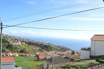 a town on a hill with the ocean in the background at Authentic Rural Retreat With Green Fields & Ocean Views - Orchid House Arco da Calheta in Calheta