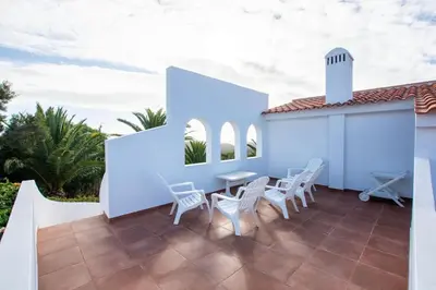 a patio with white chairs and a table and a building at A House With a View in Aljezur