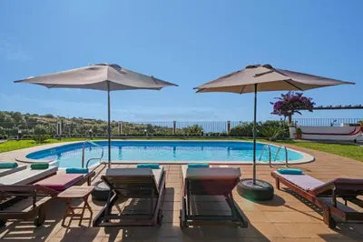 a swimming pool with chairs and umbrellas next to a pool at Villa Theos House by Villa Plus in Fajã da Ovelha